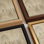 Four framed art prints arranged diagonally, showcasing different wood frame finishes: light natural wood, dark brown wood, black, and gold. The canvas feature a painting of the last supper.