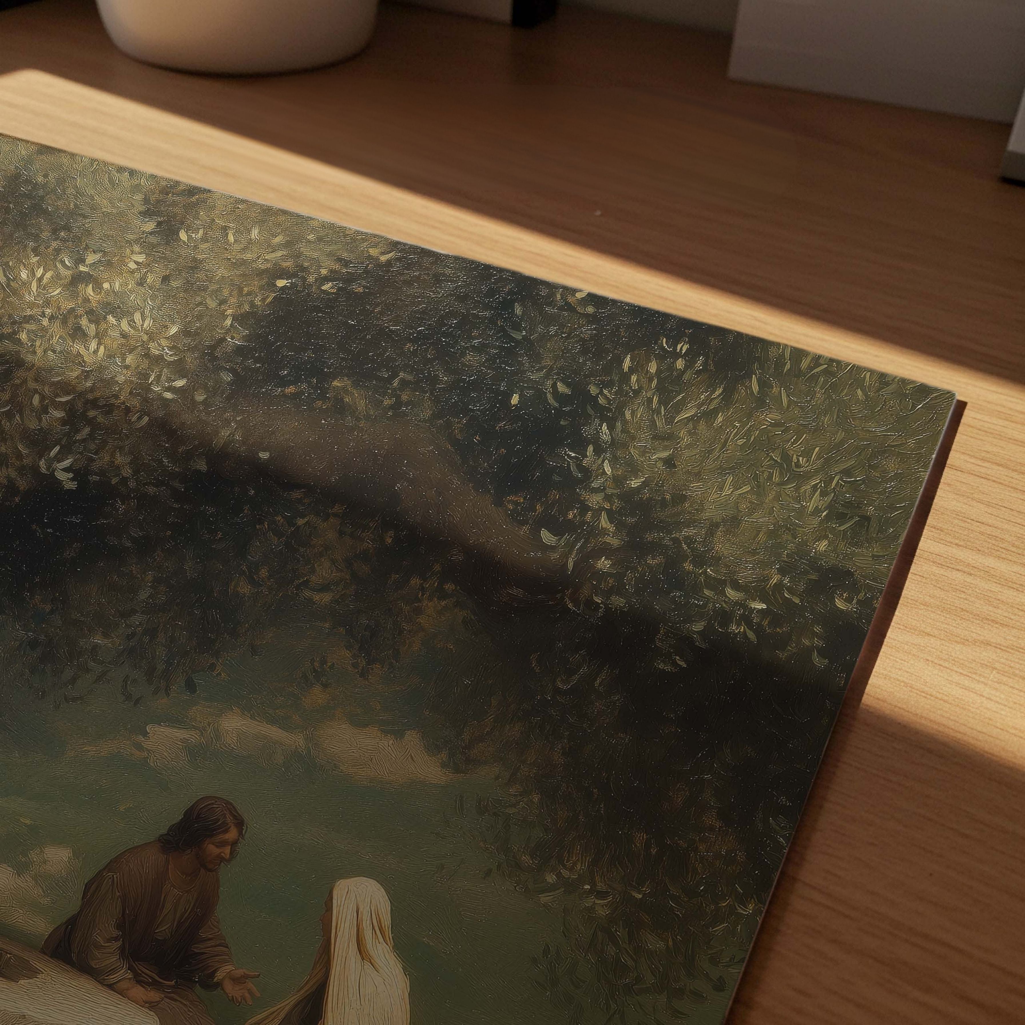 A close-up of a framed or mounted art print resting on a wooden surface, showing a painterly scene with dark trees, soft blue-green sky, and Jesus and the Samaritan woman near the bottom. The print is photographed in warm sunlight with visible shadows across it.
